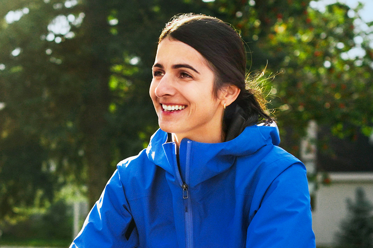 A woman wearing a blue windbreaker looking to the side and smiling